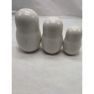 Puede incluir: Tres mu&ntilde;ecas rusas blancas, lisas y brillantes, de diferentes tama&ntilde;os, dispuestas en fila. Cada mu&ntilde;eca presenta una forma redondeada y bulbosa con una costura horizontal que separa las mitades superior e inferior, de aspecto uniforme.