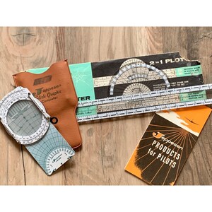 May include: A collection of vintage Jeppesen flight navigation tools, including a slide graphic computer, protractor, and a booklet titled "Products for Pilots." The items are in various colors, including brown, black, white, and orange.