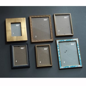 May include: Six picture frames in different sizes and colours, including gold, black, and blue. The frames are arranged in a grid pattern on a dark grey background. The frames are labelled with their dimensions in inches, such as 4x6, 5x7, and 6x8.
