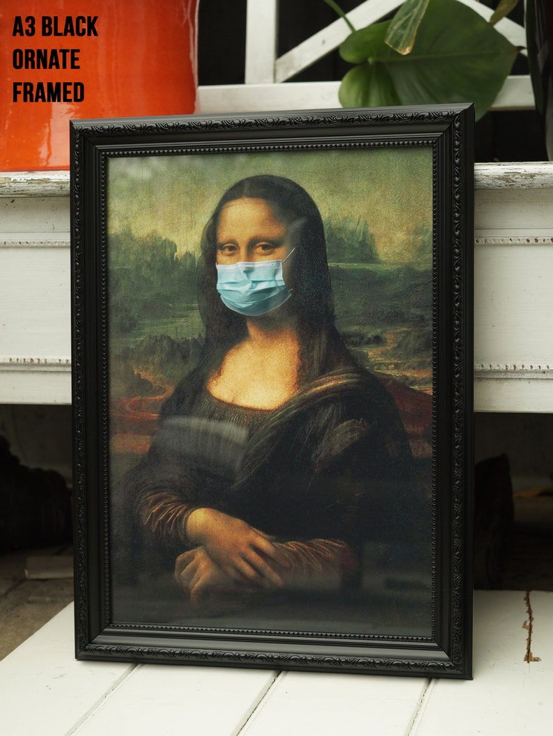 Puede incluir: Una impresi&oacute;n enmarcada en negro de la Mona Lisa con una m&aacute;scara quir&uacute;rgica azul. La impresi&oacute;n est&aacute; en un marco negro adornado.