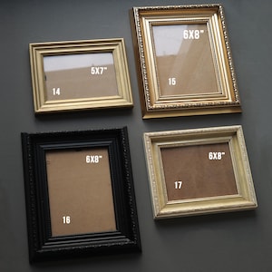 May include: Four picture frames in different sizes and colours. The frames are all gold, black, and white. The frames are all hanging on a grey wall. The frames are labelled with their sizes: 5x7", 6x8", 6x8", and 6x8".