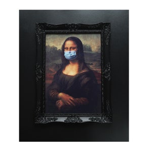 Puede incluir: Una pintura enmarcada de la Mona Lisa con una mascarilla facial azul. La pintura est&aacute; en un marco negro con detalles ornamentados.