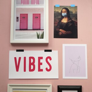 Puede incluir: Una pared rosa con impresiones enmarcadas, incluyendo una impresi&oacute;n de la Mona Lisa con una m&aacute;scara facial, una impresi&oacute;n de un edificio con dos puertas rosas, una impresi&oacute;n con la palabra "VIBES" en letras rosas, una impresi&oacute;n de un dibujo de l&iacute;nea de una cara y una impresi&oacute;n de un cartel de concierto vintage para Elvis Presley.