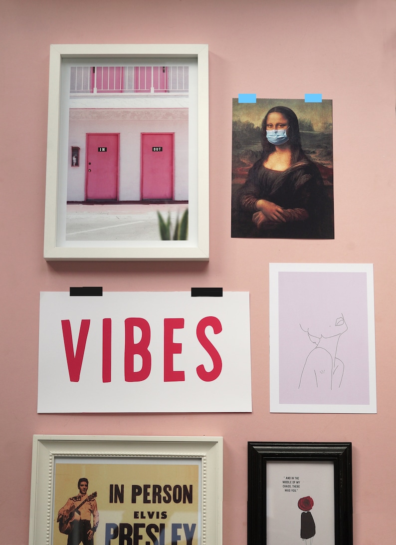 Puede incluir: Una pared rosa con impresiones enmarcadas, incluyendo una impresi&oacute;n de la Mona Lisa con una m&aacute;scara facial, una impresi&oacute;n de un edificio con dos puertas rosas, una impresi&oacute;n con la palabra "VIBES" en letras rosas, una impresi&oacute;n de un dibujo de l&iacute;nea de una cara y una impresi&oacute;n de un cartel de concierto vintage para Elvis Presley.