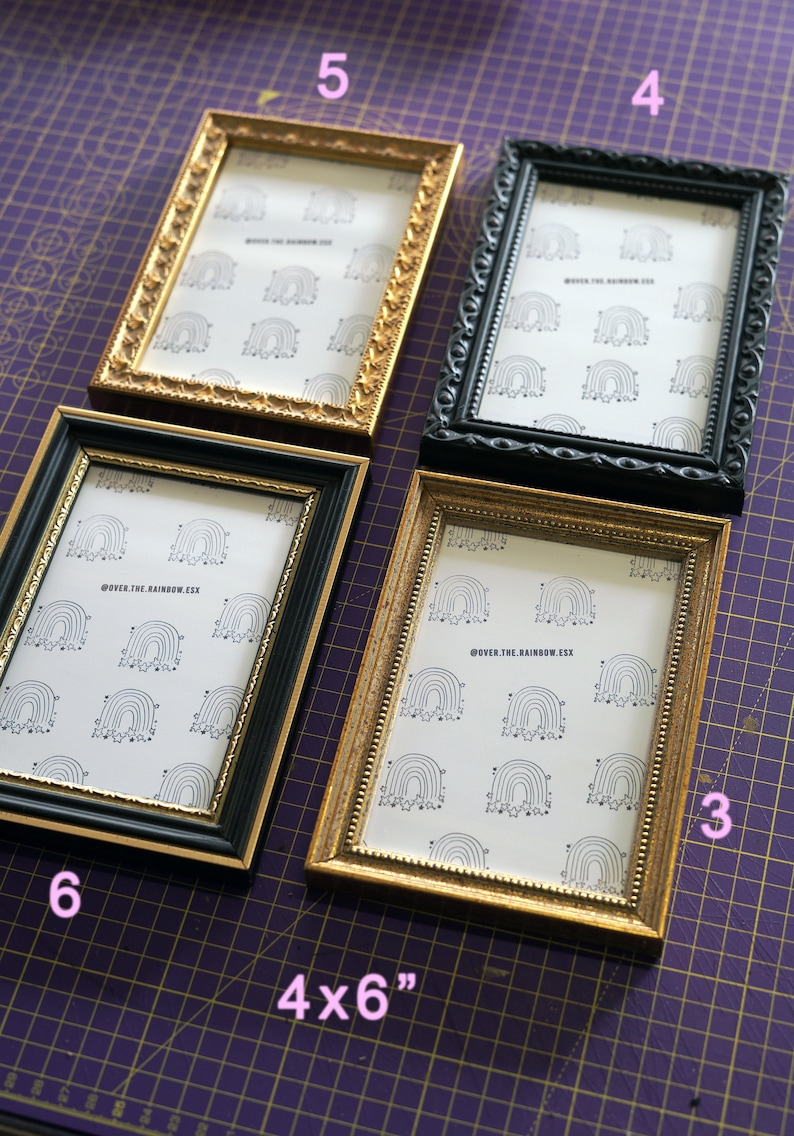 Op de afbeelding: Vier fotolijsten in verschillende stijlen en kleuren, waaronder goud en zwart. De lijsten zijn in een rij op een paarse rooster-oppervlak gerangschikt. De lijsten zijn allemaal 4x6 inch en bevatten een afdruk van een regenboog met sterren.