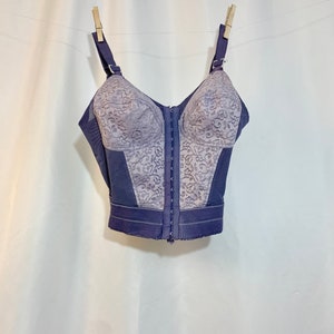 May include: A purple lace and nylon undergarment with a front zipper and hook and eye closure. The garment has a floral pattern and is hanging on a clothesline.