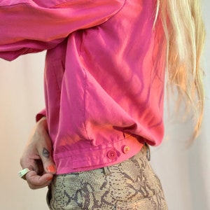 May include: A pink button-down shirt with long sleeves and a snakeskin print skirt.