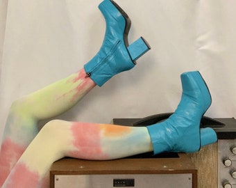 Könnte beinhalten: Ein Paar blaue Plateau-Stiefel mit einem dicken Absatz. Die Stiefel werden mit Batik-Strumpfhosen getragen und stehen auf einem Vintage-Stereo.