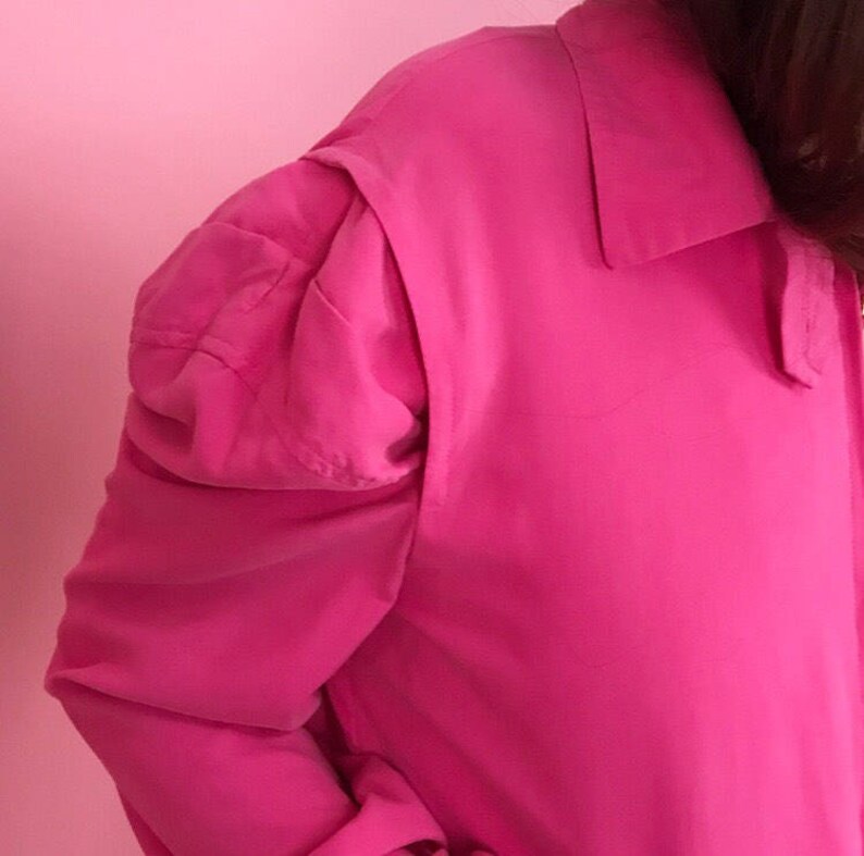 May include: A bright pink long-sleeved shirt with puffed shoulders and a collar.