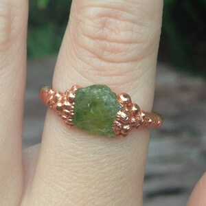 May include: Two rings with green gemstone settings. The rings are made of copper wire and have a beaded design. The gemstones are rough and irregular in shape.