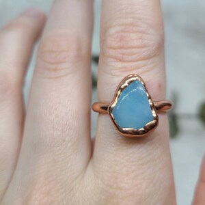 May include: A copper ring with a light blue aquamarine stone set in the centre. The ring is on a finger.