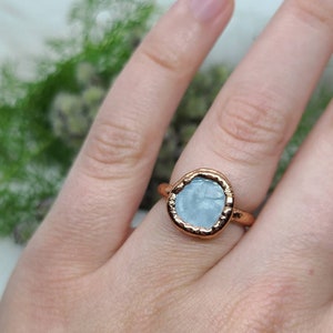Puede incluir: Un anillo de oro rosa con una piedra de aguamarina azul claro engastada en un engaste texturizado.