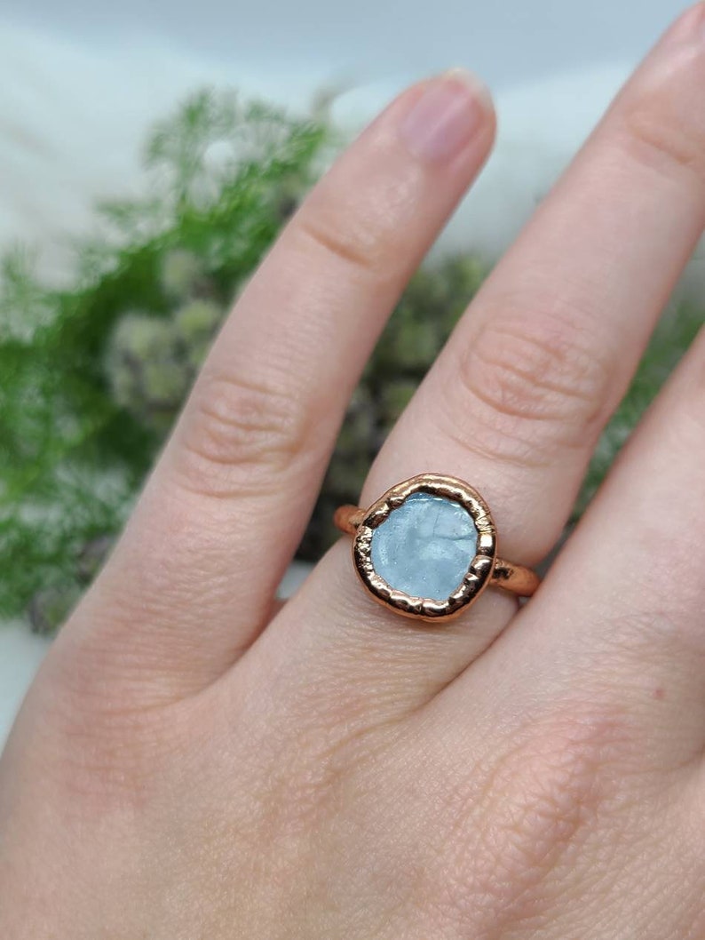 Puede incluir: Un anillo de oro rosa con una piedra de aguamarina azul claro engastada en un engaste texturizado.