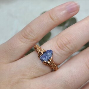 Puede incluir: Un anillo de cobre con una banda texturizada y una piedra preciosa azul engastada en el centro.