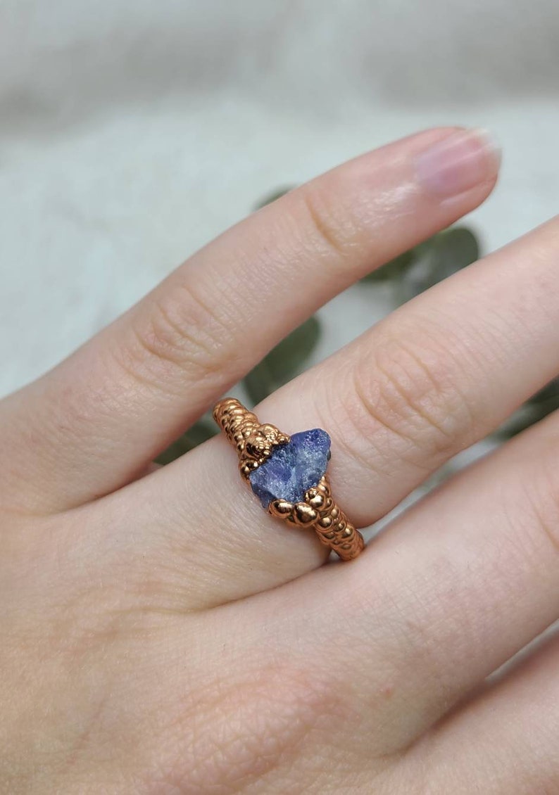 Puede incluir: Un anillo de cobre con una banda texturizada y una piedra preciosa azul engastada en el centro.