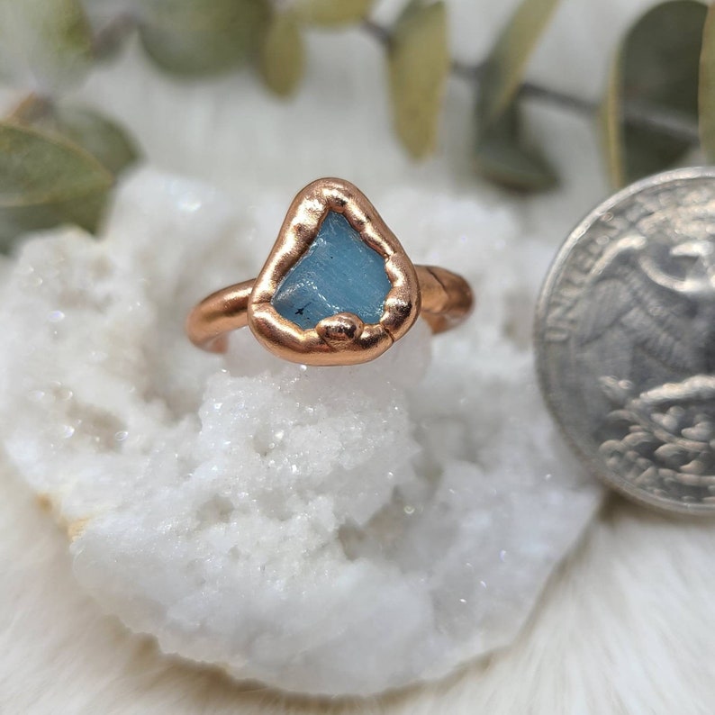 K&ouml;nnte beinhalten: Ein Kupferring mit einem hellblauen Aquamarin-Stein, der in der Mitte eingesetzt ist. Der Ring ist handgefertigt und hat einen rustikalen, organischen Look.