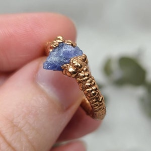 Puede incluir: Un anillo con una banda de oro texturizada y una piedra preciosa azul en bruto engastada en la banda.