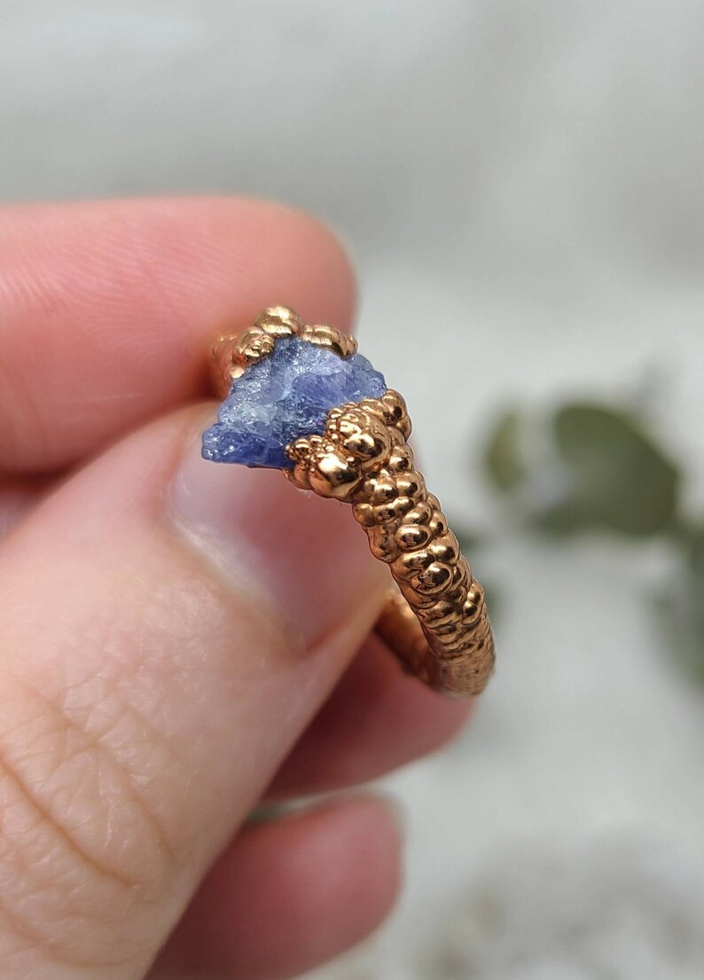 Puede incluir: Un anillo con una banda de oro texturizada y una piedra preciosa azul en bruto engastada en la banda.