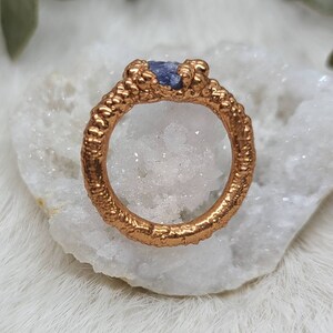 Puede incluir: Un anillo de oro con una banda texturizada y una peque&ntilde;a piedra preciosa p&uacute;rpura engastada en el centro.