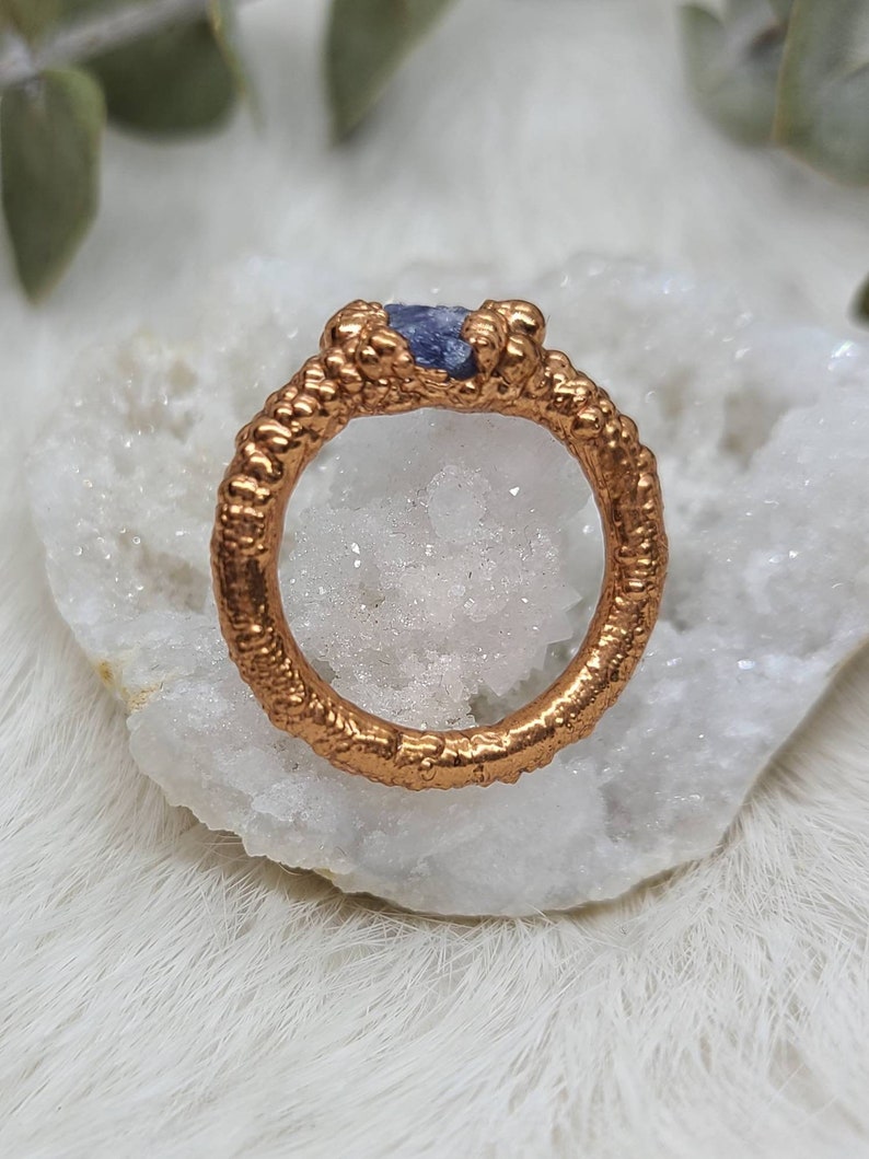 Puede incluir: Un anillo de oro con una banda texturizada y una peque&ntilde;a piedra preciosa p&uacute;rpura engastada en el centro.