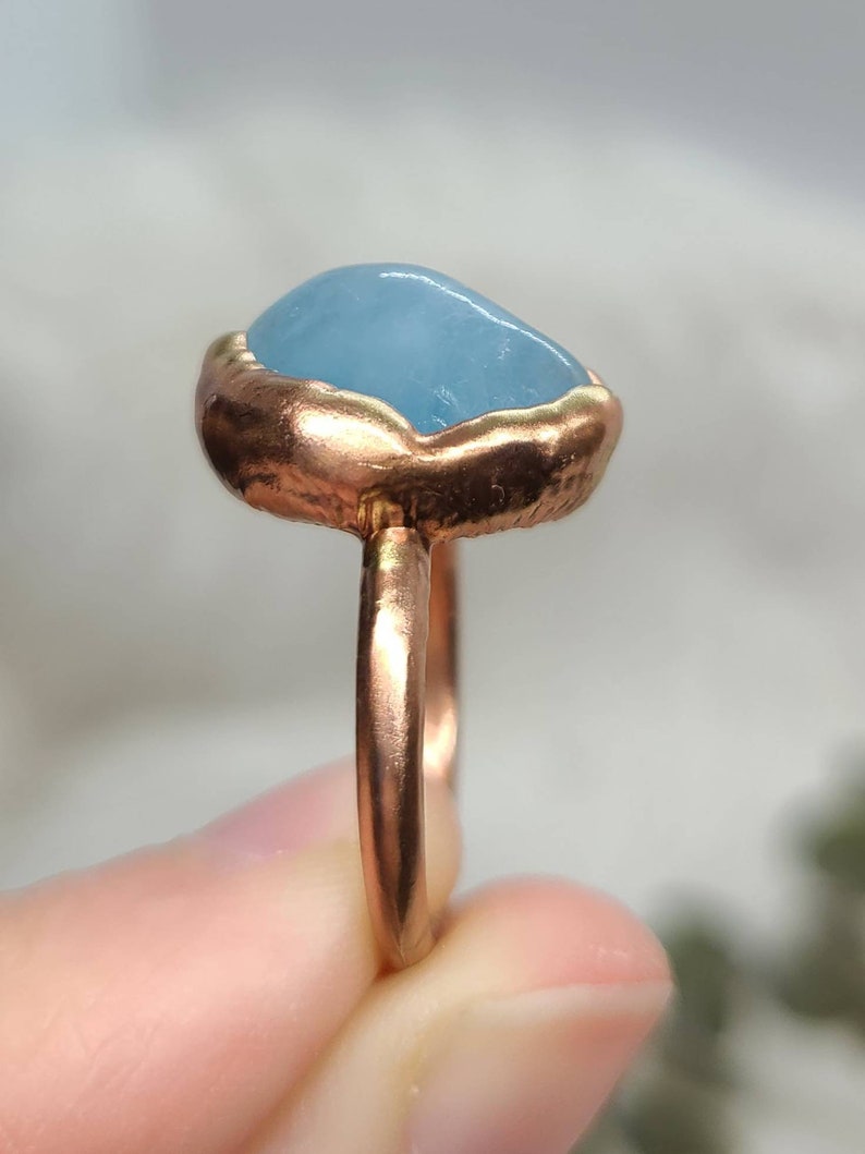 Op de afbeelding: Een ring met een lichtblauwe aquamarijn steen gezet in een koperen band.