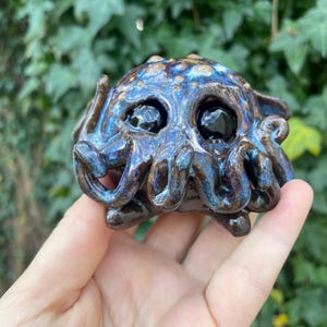 May include: A small ceramic sculpture of an octopus with blue, brown, and black glaze. The octopus has large, black eyes and a textured surface.