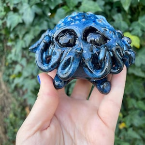 May include: A small blue and black ceramic sculpture of a creature with multiple tentacles and large eyes.
