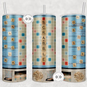May include: A stainless steel tumbler featuring a Scrabble game design. The design includes a light blue wood-look background with Scrabble tiles and a game board. The tumbler has a silver straw and a lid. The words "LETS PLAY" are visible.