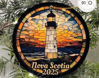 May include: A round black-framed ornament featuring a stained-glass style image of a lighthouse at sunset. The design includes a glowing lantern room, a rocky coastline, and the text Nova Scotia 2025 printed in a serif font at the bottom.