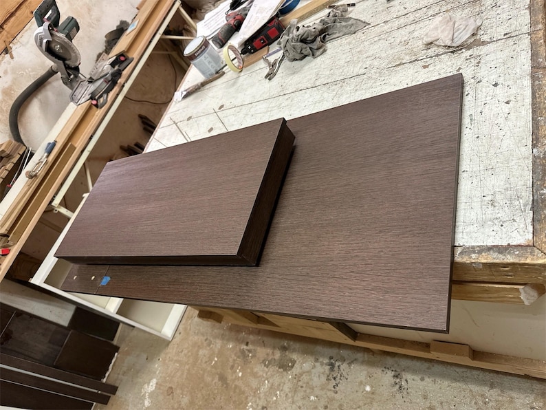 Pu&ograve; includere: Due tavole rettangolari in legno marrone scuro con una texture venata visibile. La tavola pi&ugrave; piccola &egrave; posizionata sopra quella pi&ugrave; grande, entrambe presentano bordi dritti e puliti e una superficie piatta e liscia color espresso.