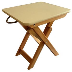 Puede incluir: Una mesa plegable de madera marr&oacute;n claro con una tapa beige. La mesa tiene un asa de cuerda y est&aacute; hecha de madera natural.