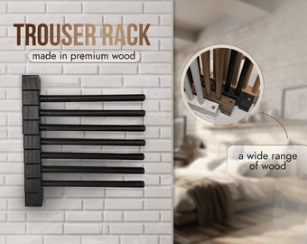 May include: A black wooden trouser rack mounted on a white brick wall. The rack has eight black metal rods for hanging trousers. The text "TROUSER RACK" and "made in premium wood" is displayed above the rack.