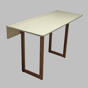 Könnte beinhalten: Ein weißer Klapptisch mit einem Holzrahmen. Der Tisch ist geschlossen und hat ein kleines Regal an der Seite.