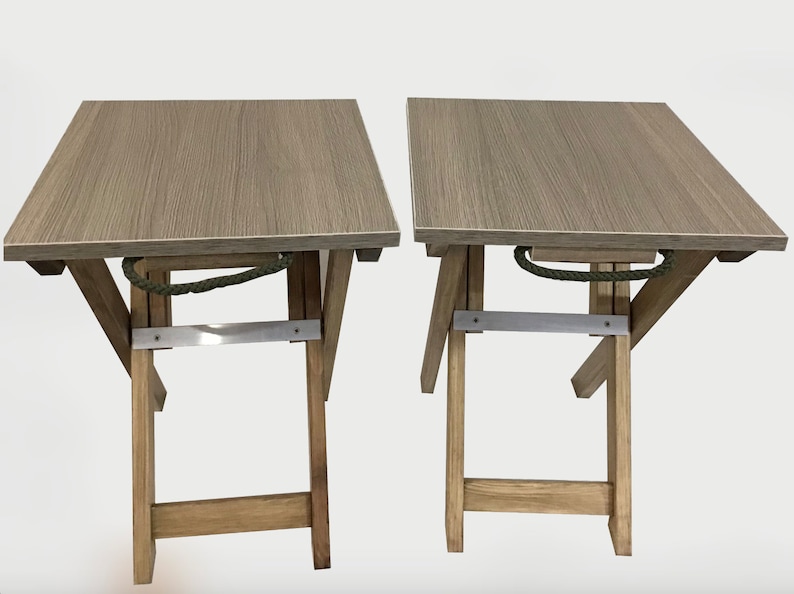 Puede incluir: Dos mesas plegables de madera con un acabado de grano de madera marr&oacute;n claro. Las mesas tienen un asa de cuerda y una abrazadera de metal.
