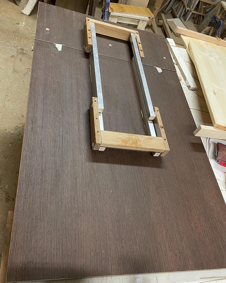 Pu&ograve; includere: Un pannello rettangolare in laminato con venature del legno marrone scuro, caratterizzato da un telaio centrale in metallo e legno chiaro. Il telaio &egrave; composto da due binari metallici argentati paralleli collegati da due traverse in legno chiaro.