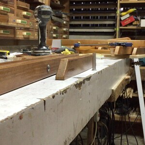 Puede incluir: Un primer plano de un banco de trabajo de madera con una variedad de herramientas y materiales. El banco de trabajo est&aacute; hecho de madera de color claro y tiene una superficie pintada de blanco. Hay varias herramientas y materiales en el banco de trabajo, incluyendo un taladro, una sierra, una cinta m&eacute;trica y una pieza de madera.