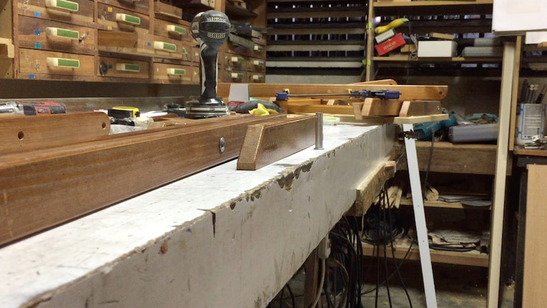 Puede incluir: Un primer plano de un banco de trabajo de madera con una variedad de herramientas y materiales. El banco de trabajo est&aacute; hecho de madera de color claro y tiene una superficie pintada de blanco. Hay varias herramientas y materiales en el banco de trabajo, incluyendo un taladro, una sierra, una cinta m&eacute;trica y una pieza de madera.