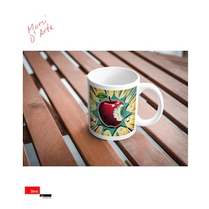 May include: White ceramic mug featuring a red apple with a bite taken out of it. The apple is surrounded by a yellow, blue and green comic book style explosion. The text "Morsi D'Arte" is written in red at the top of the mug.