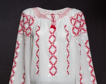 May include: White long-sleeved blouse with intricate red embroidery. The blouse features a round neckline with delicate lace trim and a tassel tie. The sleeves are wide and flared, with red tassels at the cuffs. The embroidery includes floral and geometric patterns.