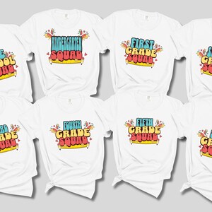 May include: White t-shirts with colorful text designs. Each shirt features a grade level, such as "Pre-School Squad," "First Grade Squad," or "Sixth Grade Squad." The text is in a retro font with a pencil and starburst design.