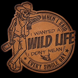 May include: A brown leather patch with a cowboy skeleton graphic. The skeleton leans against a circular design with the text "WHEN I SAID I WANTED A WILD LIFE I DIDN'T MEAN EVERY SINGLE DAY". A bottle and bull skull are also featured.
