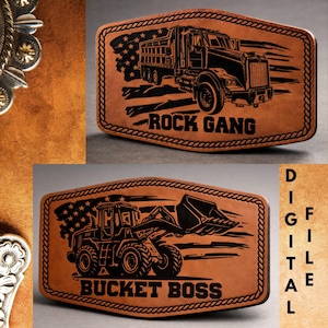 May include: Two brown leather belt buckles with black engraved designs. One features a dump truck with the text "ROCK GANG", and the other shows a front-end loader with "BUCKET BOSS". Both have a rope-like border and an American flag.