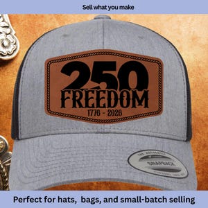 May include: Gray trucker hat with a black mesh back and a brown leather patch. The patch features the number "250" above the word "FREEDOM" and the dates "1776-2026". The hat has a snapback closure.