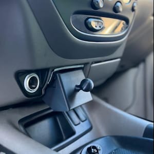 Può includere: Un supporto nero e angolato per telefono da auto installato nel cruscotto di un veicolo. Il supporto è dotato di un giunto sferico per regolare la posizione del telefono ed è progettato per adattarsi alla console del veicolo. Il cruscotto circostante è grigio.