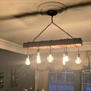 May include: A rustic wooden chandelier with six Edison bulb lights hanging from a black chain. The chandelier is suspended from a ceiling with a decorative medallion.