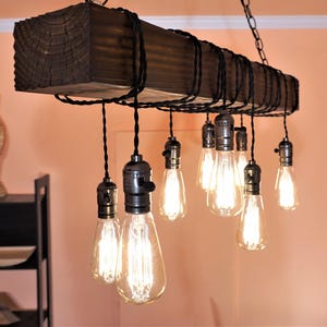 May include: A rustic wooden chandelier with a dark brown finish and exposed wiring. It features multiple Edison bulb light fixtures hanging from the wood beam.