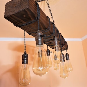 May include: A rustic wooden chandelier with eight Edison bulb lights hanging from black cords. The chandelier is made from a reclaimed wood beam and has a simple, industrial design.