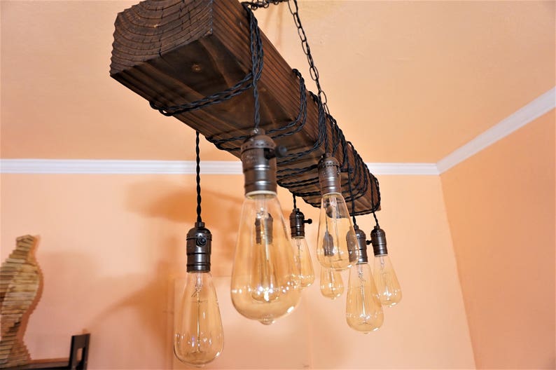 May include: A rustic wooden chandelier with eight Edison bulb lights hanging from black cords. The chandelier is made from a reclaimed wood beam and has a simple, industrial design.