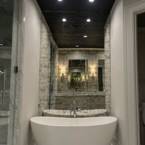 Puede incluir: Una ba&ntilde;era exenta ovalada de color blanco con un grifo cromado centrado en el borde. La ba&ntilde;era est&aacute; situada contra una pared cubierta con grandes paneles de espejo de acabado antiguo y desgastado que reflejan el ba&ntilde;o y las luces del techo.