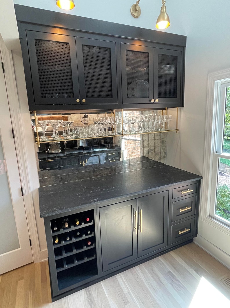 May include: A black home bar cabinet featuring upper cabinets with mesh panels, a mirrored backsplash, and gold hardware. The unit includes a black countertop, a built-in wine rack, two lower cabinet doors, and three drawers with gold handles.